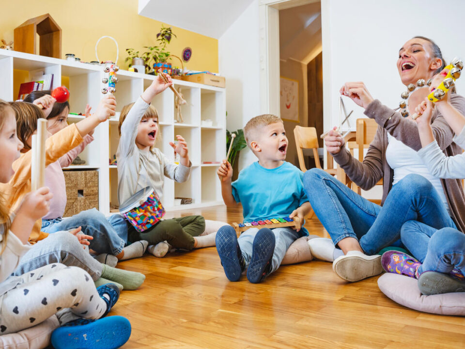 Kindergarten teacher with children sitting on the floor having music class, using various instruments and percussion.