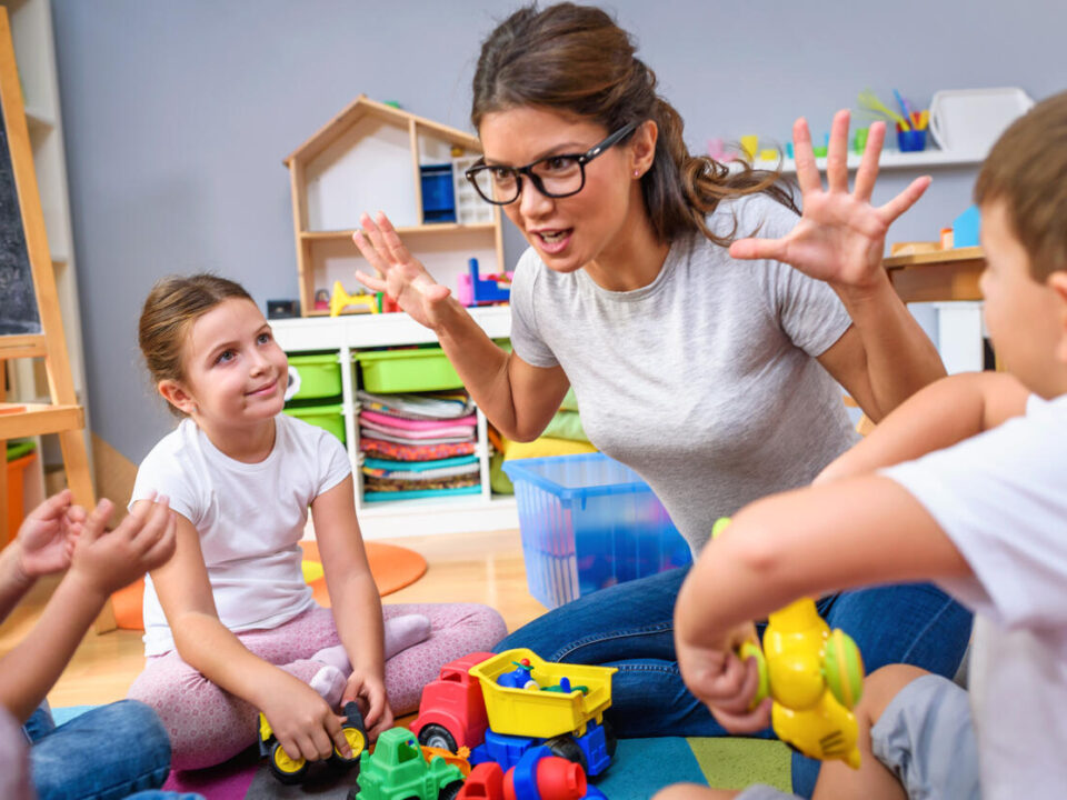 Preschool teacher talking to group of children sitting on a floor at kindergarten