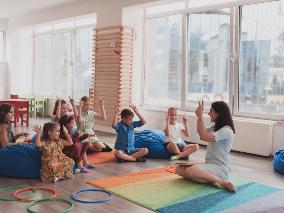 A happy female teacher sitting and playing hand games with a group of little schoolchildren